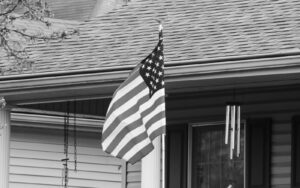 American flag displayed on suburban front porch near wind chimes