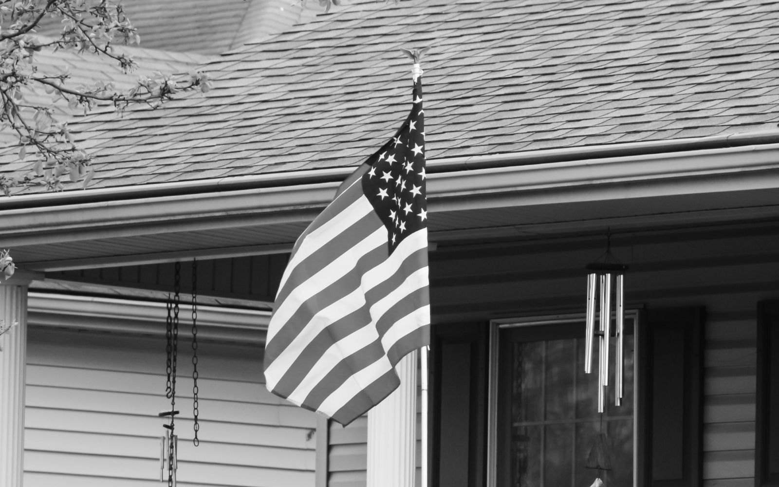 American flag displayed on suburban front porch near wind chimes