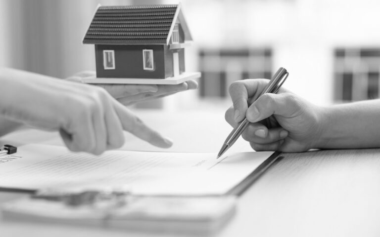 Person signing a leaseback agreement with a miniature house model on the table.