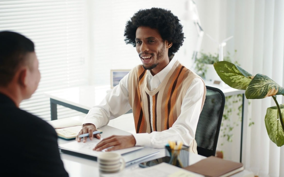 A smiling property manager talking to a client across a desk in a bright, plant-filled office.