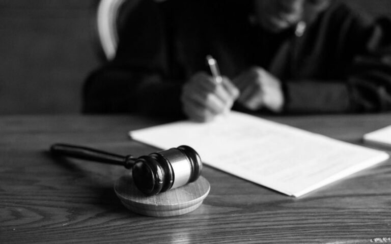 Close-up of a judge’s gavel on a desk with a person writing in the background, symbolising a legal ruling.