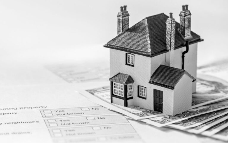 A miniature house on top of property documents and dollar bills, representing real estate data used for property valuation and market analysis.