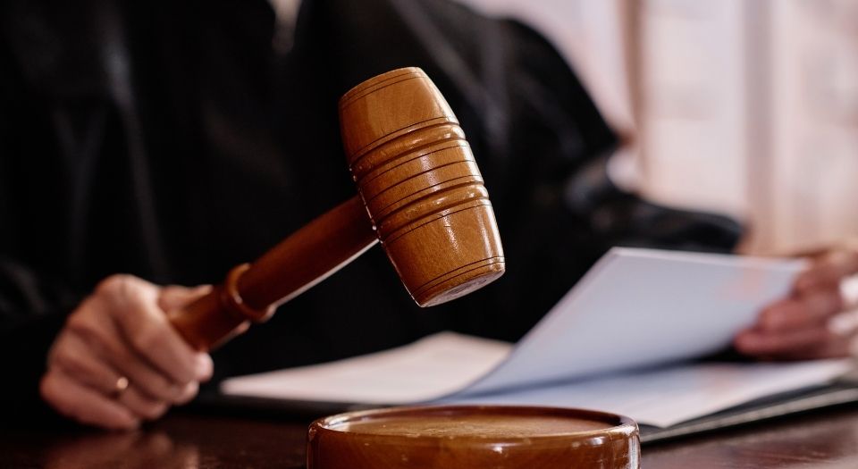 A close-up of a judge’s wooden gavel being held above a sound block in a courtroom, symbolizing legal rulings and antitrust actions in the real estate sector.